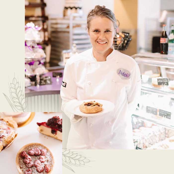 Smiling chef holding a pastry in a bakery café, with desserts and cakes visible in the background.